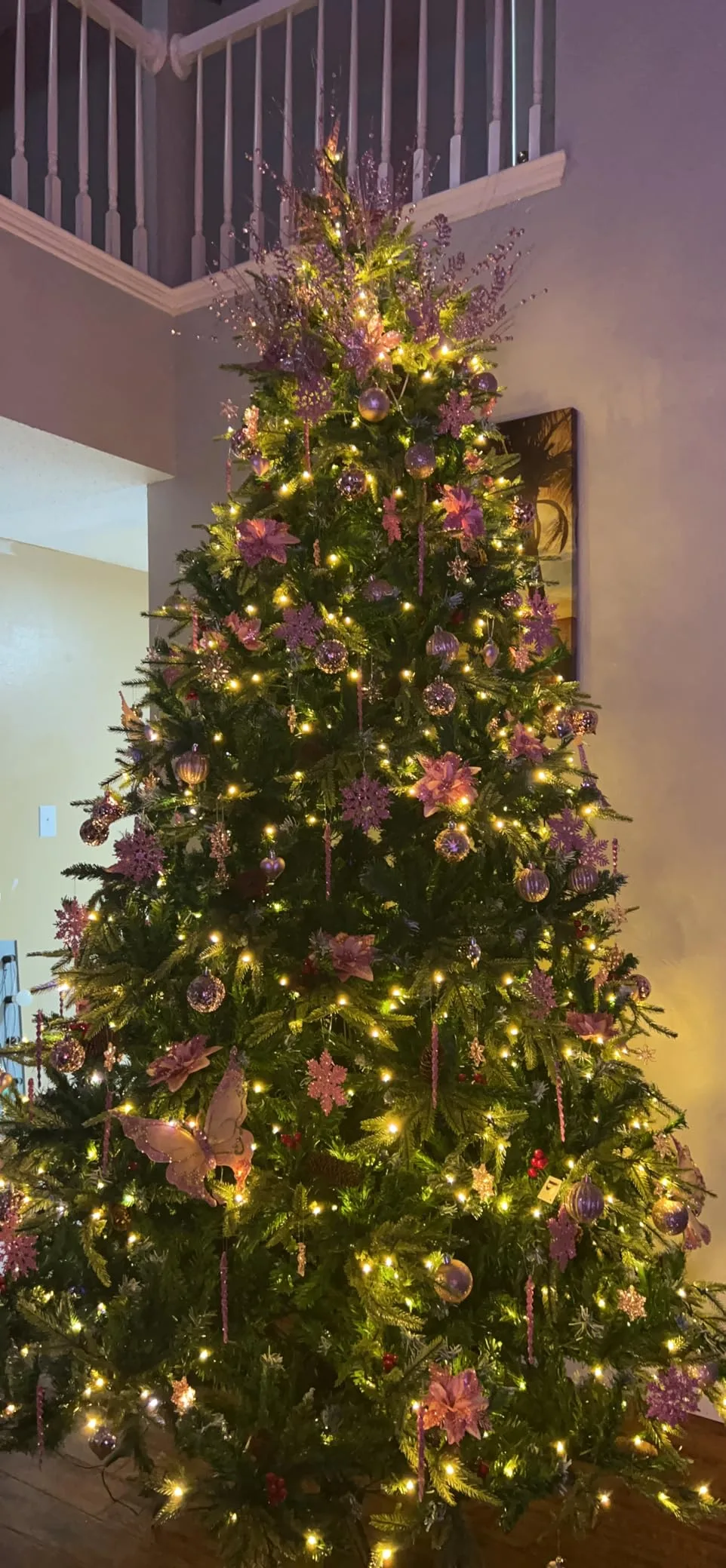 Beautiful Designer Christmas Decor Dupes You Can Buy or DIY – Natural Christmas Tree with Golden Accents

A green Christmas tree is illuminated with warm golden lights and decorated with natural-looking branches, gold accents, and a large metallic bow. The layered greenery and shimmering ornaments create a warm, woodland-inspired holiday style with plenty of texture.