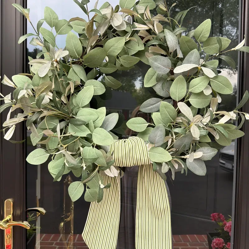 Easy Ways to Make Your Porch Feel Like Fall - Greenery Wreath with Striped Bow: A close-up of a lush green wreath made with rounded leaves, finished with a large cream-and-green striped ribbon bow against a dark front door.