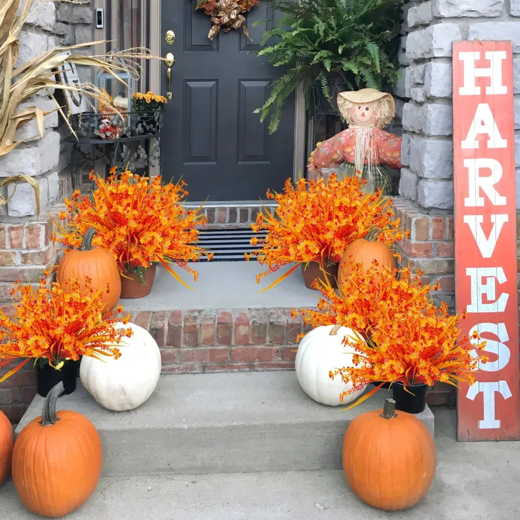 Easy Ways to Make Your Porch Feel Like Fall - Fall porch decor featuring orange foliage, orange and white pumpkins, a small scarecrow, and a harvest sign beside a black front door.