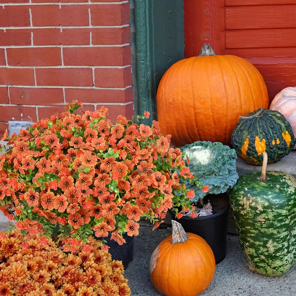 Easy Ways to Make Your Porch Feel Like Fall - Large orange pumpkins, colorful fall mums, and ornamental cabbage arranged beside a red brick wall and green doorway.