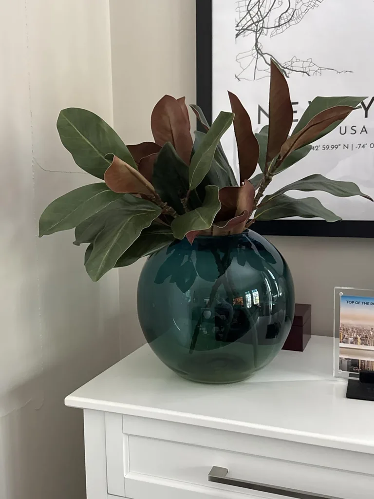 Refresh Your Living Room for Fall in 7 Easy Ways – A dark teal glass vase filled with leafy branches decorates a white side table, adding a rich green accent and a natural touch to a neutral living room.