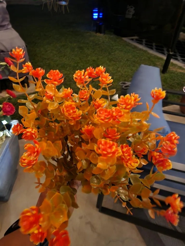 Easy Autumn Porch Decorating Ideas To Try - A close-up of orange and golden-yellow artificial autumn flowers in full bloom, arranged in a planter on an outdoor patio.