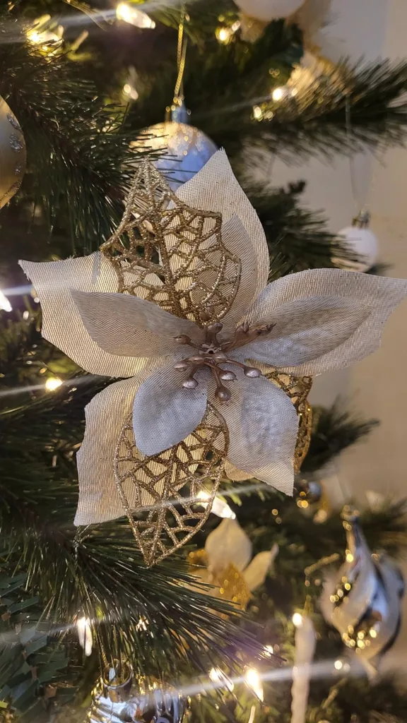 Beautiful Designer Christmas Decor Dupes You Can Buy or DIY – A close-up of a white and gold butterfly ornament nestled among evergreen branches and warm string lights showcases an elegant Christmas decoration with delicate details.