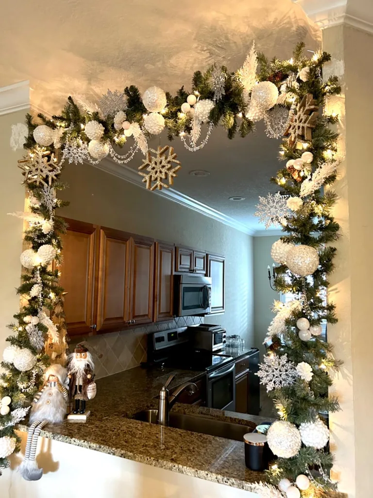 Beautiful Designer Christmas Decor Dupes You Can Buy or DIY – A traditional brick fireplace with a wooden mantel features cascading evergreen garland, cream stockings, and small seasonal accents against a deep teal wall for a cozy, sophisticated Christmas look.