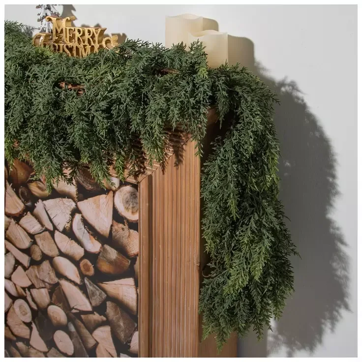 Beautiful Designer Christmas Decor Dupes You Can Buy or DIY – A rustic wooden mantel with a stacked-log pattern is topped with cascading evergreen garland and small gold decorations, creating a festive display with natural textures and classic Christmas details.