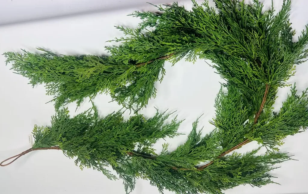 Beautiful Designer Christmas Decor Dupes You Can Buy or DIY – A close-up of lush evergreen branches arranged into a curved garland highlights the rich green foliage and natural texture of a classic Christmas decoration.