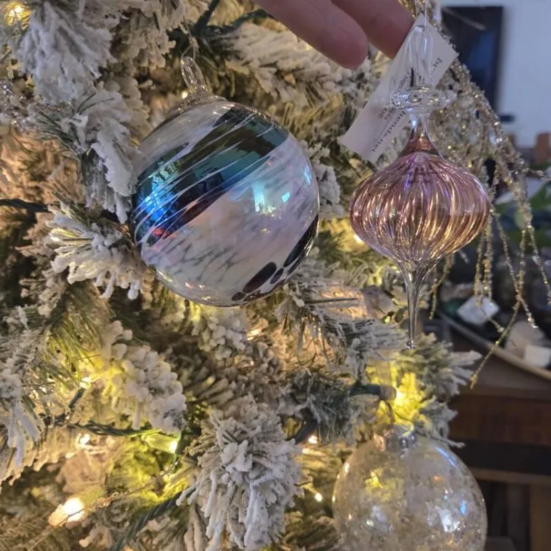 Beautiful Designer Christmas Decor Dupes You Can Buy or DIY – Iridescent Glass Christmas Baubles

Shimmering glass Christmas baubles in blue, lavender, and silver hang among snow-dusted evergreen branches. Their iridescent surfaces reflect the surrounding lights, adding a soft, whimsical touch to a winter-inspired Christmas tree.
